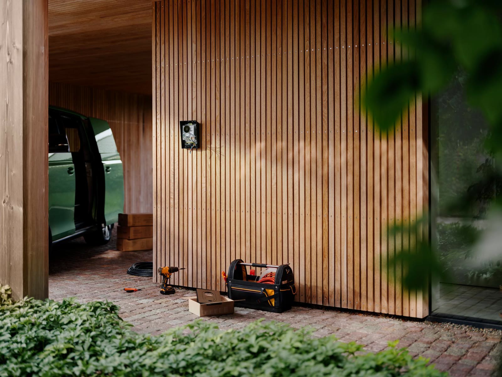 Carregador de parede recém-instalado na garagem de uma casa, com caixa de ferramentas e parafusadeira no chão